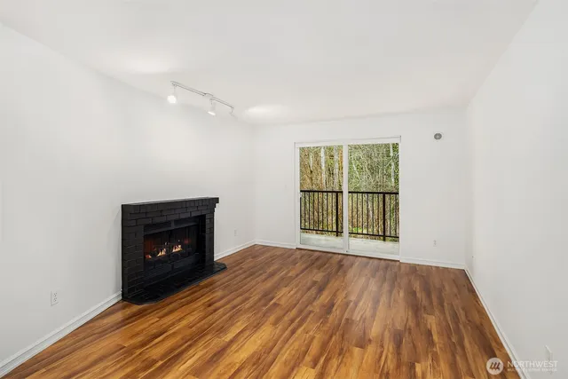 a view of an empty room with wooden floor fireplace and a window
