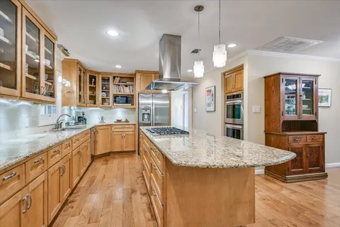 a kitchen with stainless steel appliances granite countertop a kitchen island a stove a sink dishwasher a dining table and chairs with wooden floor