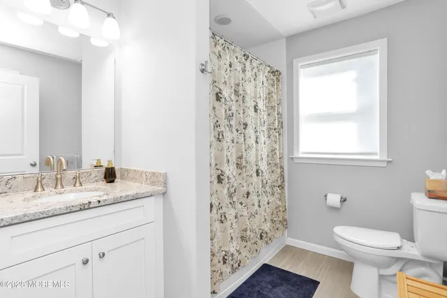 a bathroom with a granite countertop toilet a sink a mirror a shower and a window