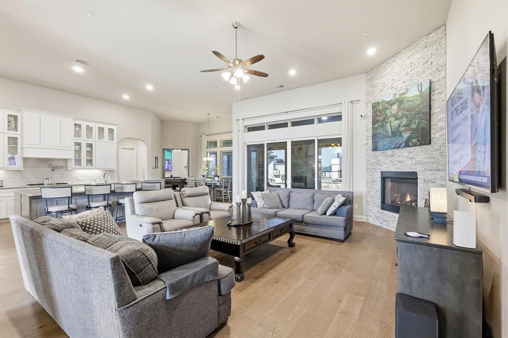 7751 Faught Road Northlake, TX 76226 - Photo 11 of 39 Spacious open-concept living area featuring light wood-finish flooring, a stone accent wall with a built-in fireplace, and expansive sliding glass doors