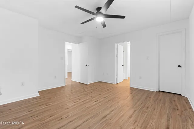 a view of an empty room with wooden floor and a ceiling fan