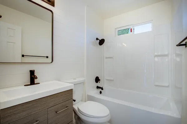 a bathroom with a bathtub shower sink vanity mirror and toilet