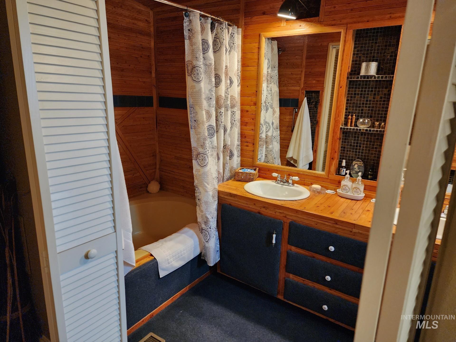 235 5th Street Grand View, ID 83624 - Photo 15 of 22 Bathroom featuring wood-finish paneling, a built-in vanity with a drop-in sink, and a combination tub and shower