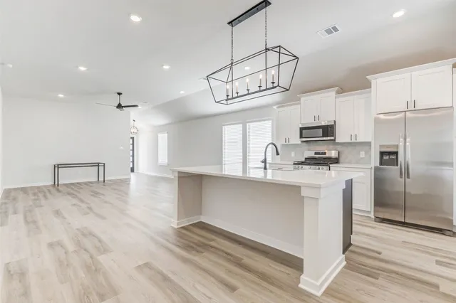 a kitchen with kitchen island stainless steel appliances a table chairs refrigerator and microwave