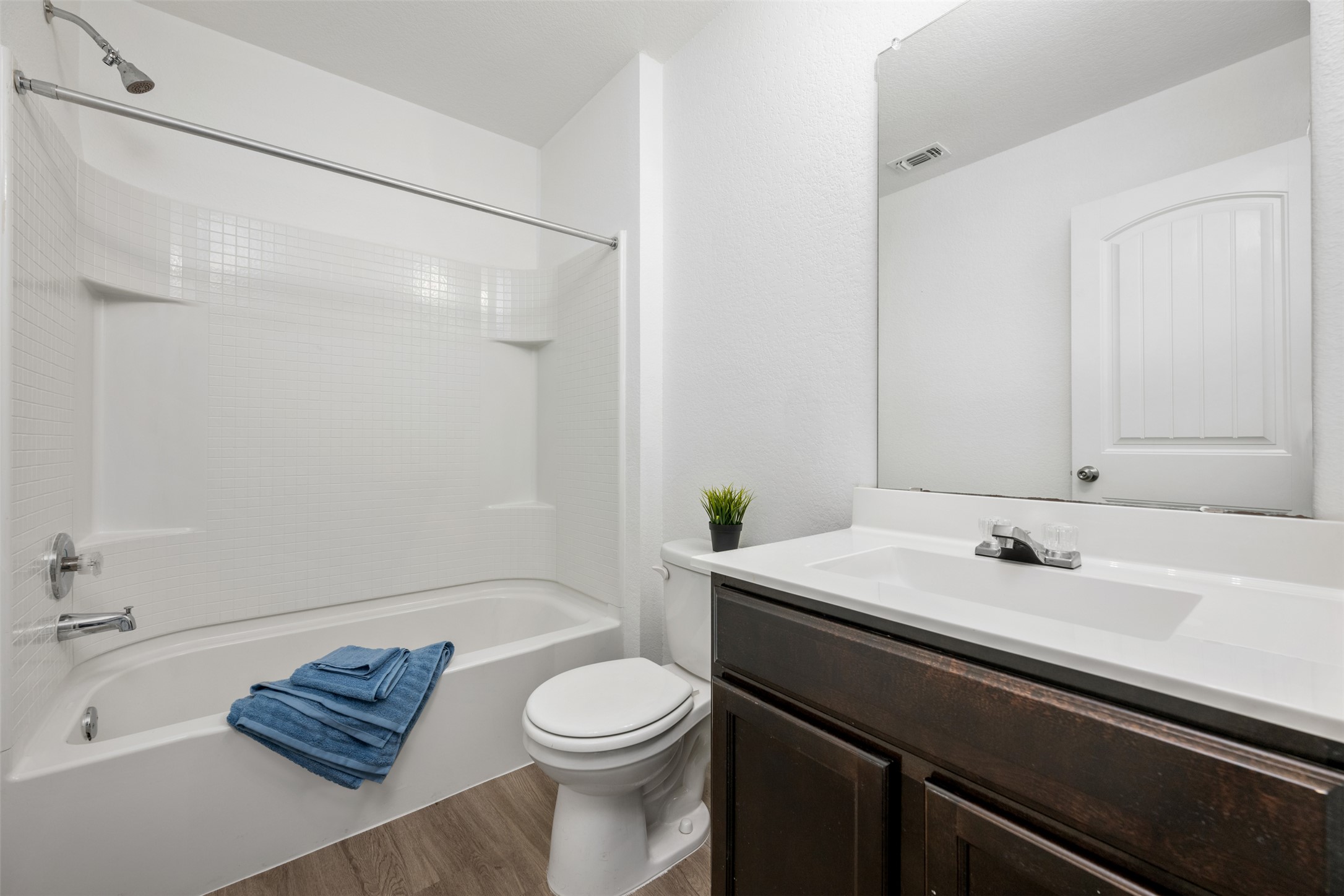 14900 Retha Pass Austin, TX 78725 - Photo 24 of 39 Full bathroom featuring a white tub and shower combination with a tiled surround, wood-finish flooring, a dark wood-finish vanity with an integrated sink, and a framed mirror