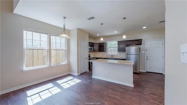 a kitchen with stainless steel appliances granite countertop a refrigerator a sink a stove and white cabinets with wooden floor