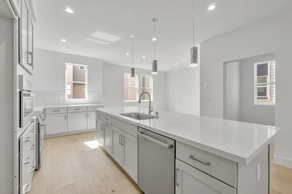 a large white kitchen with a sink and dishwasher with a large kitchen island