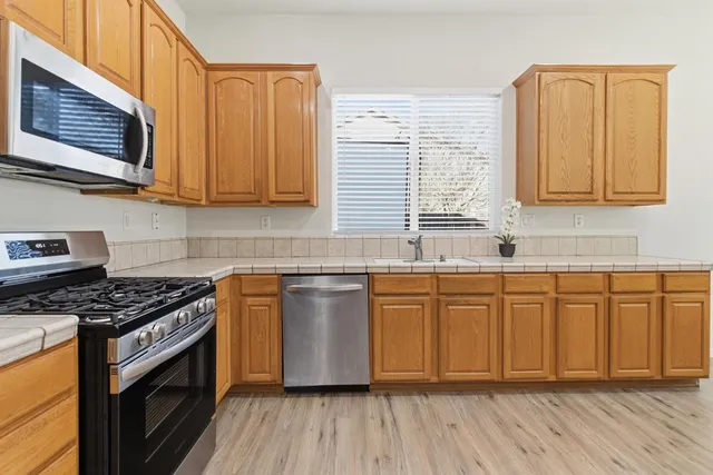 a kitchen with stainless steel appliances granite countertop a stove a sink and dishwasher wooden cabinets with wooden floor