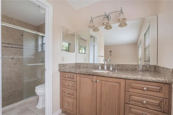 a bathroom with a granite countertop sink a toilet a mirror and shower