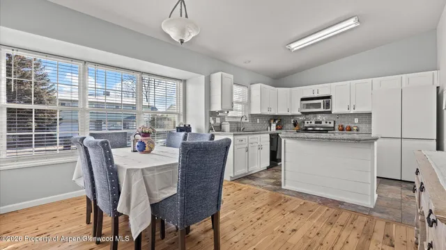 a kitchen with stainless steel appliances granite countertop a stove a refrigerator a sink dishwasher a dining table and chairs with wooden floor