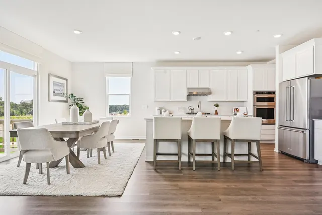 a living room with stainless steel appliances kitchen island granite countertop a dining table chairs and a refrigerator