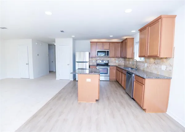 a large kitchen with stainless steel appliances granite countertop a stove a sink a refrigerator and white cabinets with wooden floor