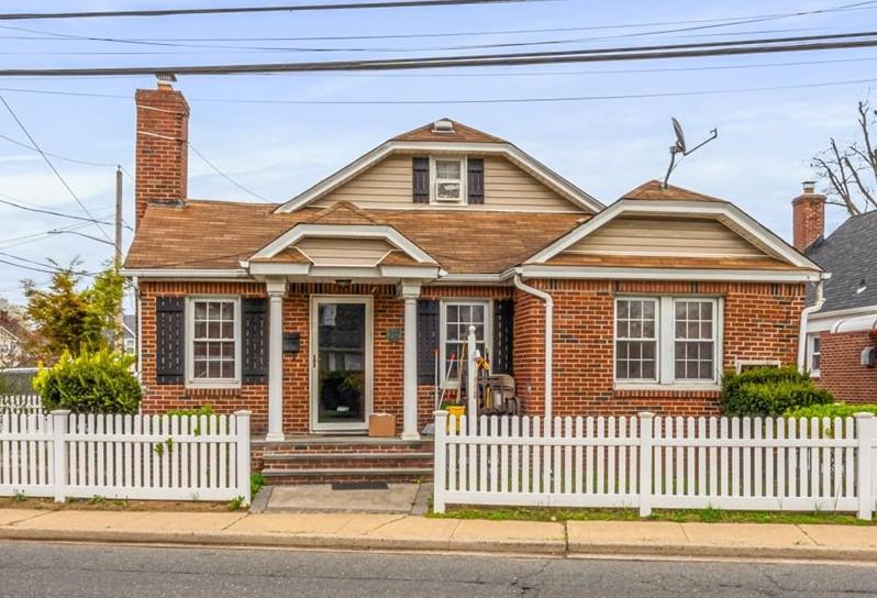 View of front facade featuring a chimney, brick siding, and a fenced front yard