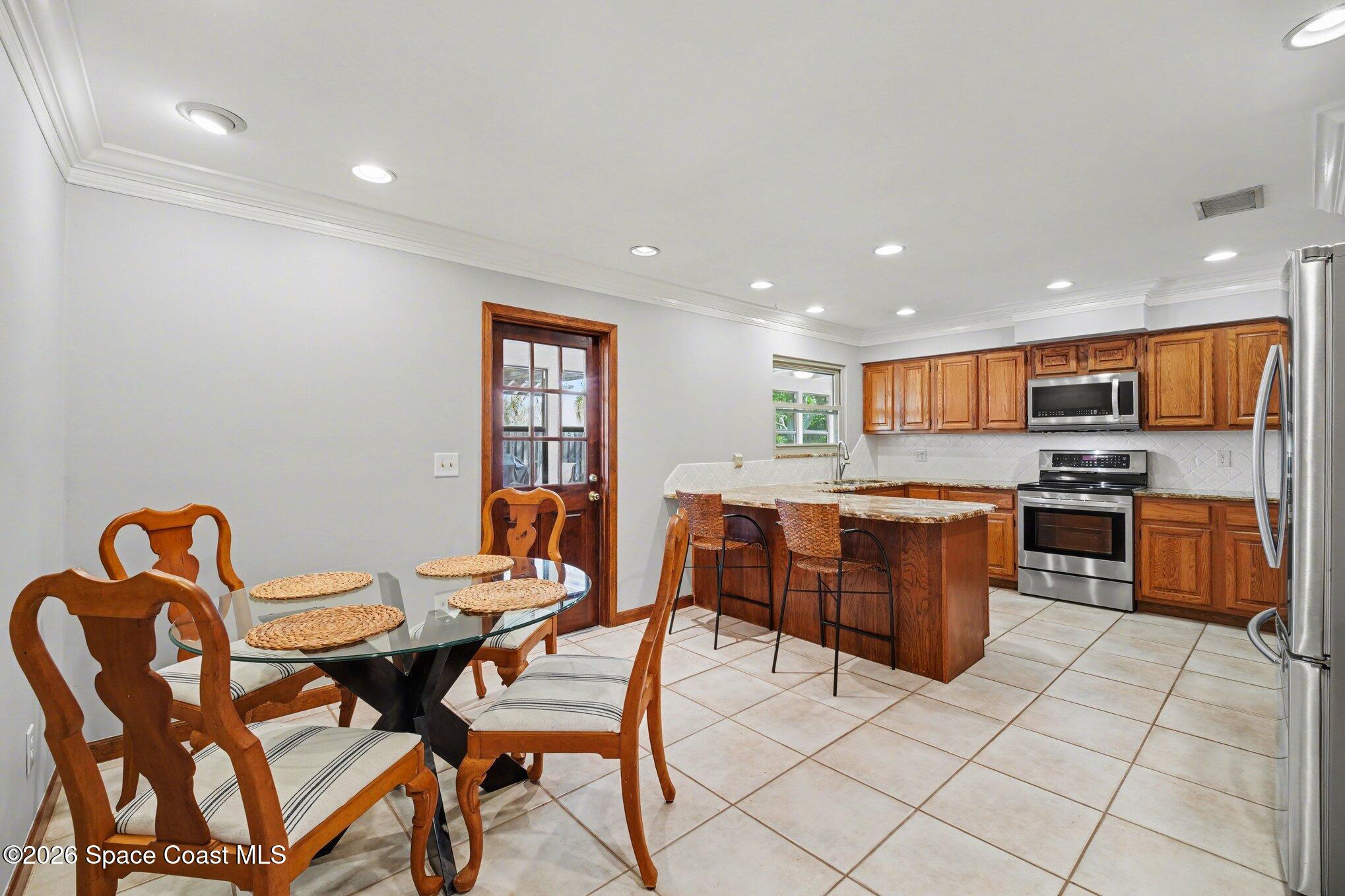 568 Rio Casa Drive North Indialantic, FL 32903 - Photo 10 of 45 a open dining room with stainless steel appliances kitchen island granite countertop a dining table chairs and a refrigerator