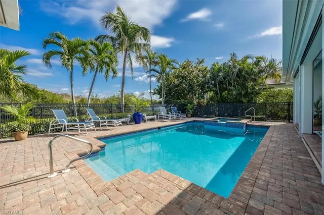 a view of swimming pool that has lawn chairs potted plants and palm trees