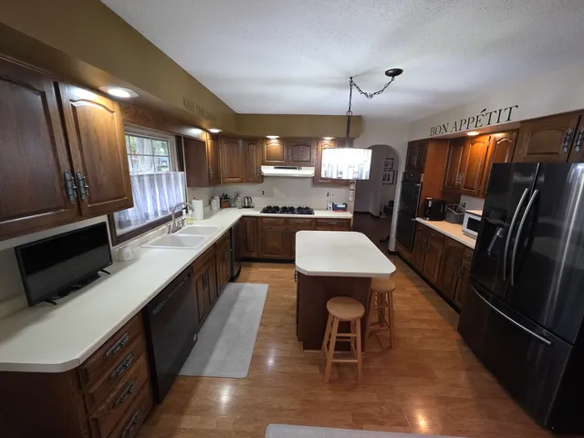 a kitchen with stainless steel appliances a stove a refrigerator a sink a dining table and chairs with wooden floor