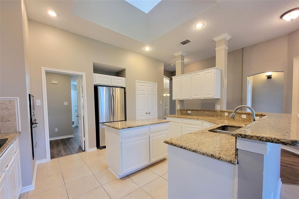 1604 Knoll Ridge Circle Corinth, TX 76210 - Photo 18 of 37 Spacious kitchen featuring an island, light-toned tile flooring, granite countertops, white cabinetry, and a skylight