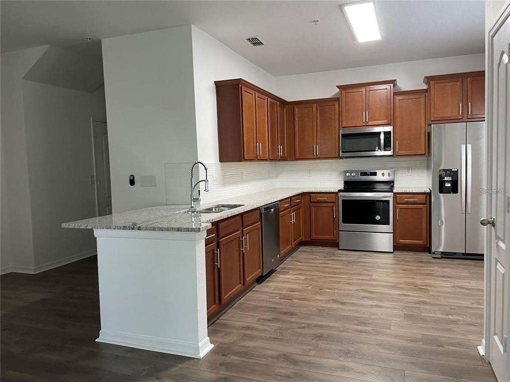 3731 Seneca Club Loop, Unit B Orlando, FL 32808 - Photo 5 of 32 a kitchen with stainless steel appliances granite countertop a stove top oven a sink dishwasher and a refrigerator with wooden floor