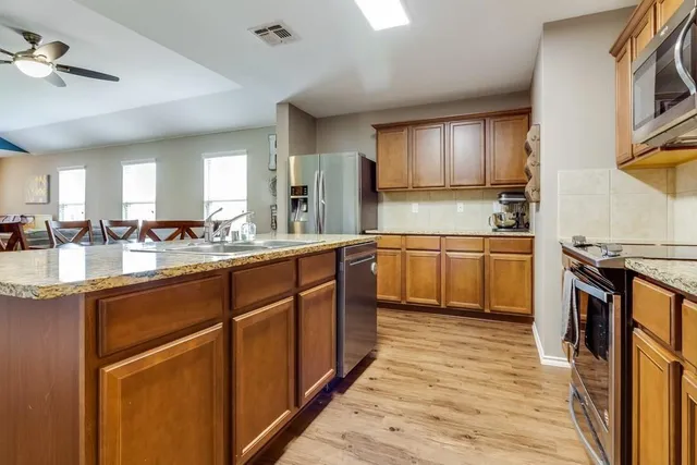 a large kitchen with stainless steel appliances granite countertop a sink dishwasher stove and wooden cabinets