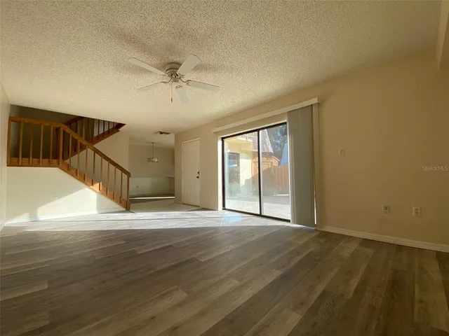 a view of an empty room with wooden floor and a ceiling fan