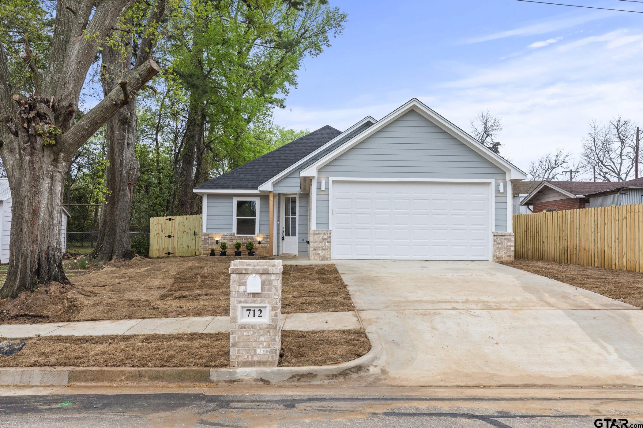 a view of a house with a yard plants and large tree
