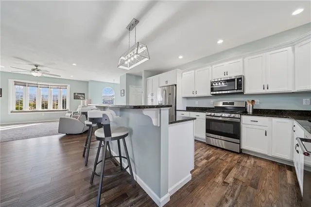 a kitchen with stainless steel appliances kitchen island granite countertop a stove top oven a sink a dining table and chairs with wooden floor