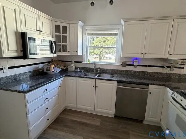 a kitchen with granite countertop white cabinets sink and a window