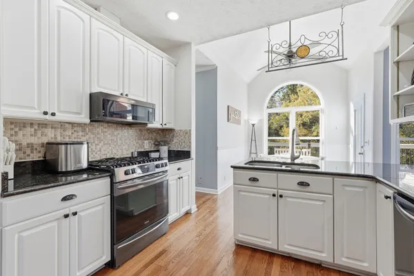 a kitchen with stainless steel appliances granite countertop a stove a sink and a white cabinets with wooden floor