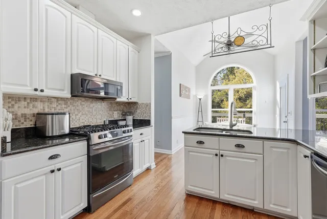 a kitchen with stainless steel appliances granite countertop a stove a sink and a white cabinets with wooden floor