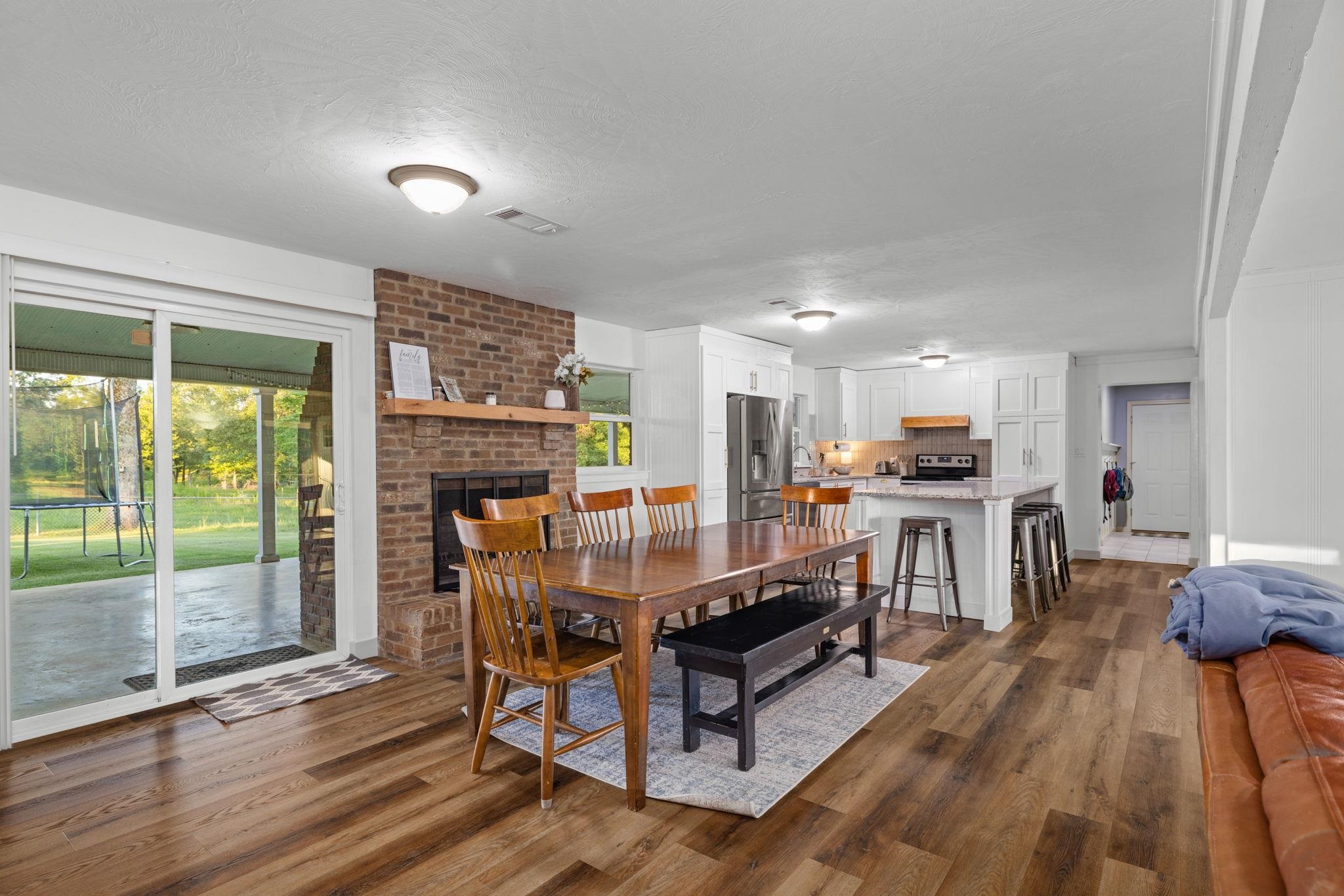66 County Road 511 Corinth, MS 38834 - Photo 8 of 40 Spacious living area featuring wood-finish flooring, a brick fireplace with a wood mantle, and sliding glass doors opening to a covered patio