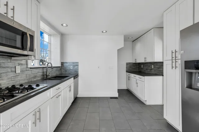 a kitchen with stainless steel appliances a stove a microwave a sink a refrigerator and white cabinets