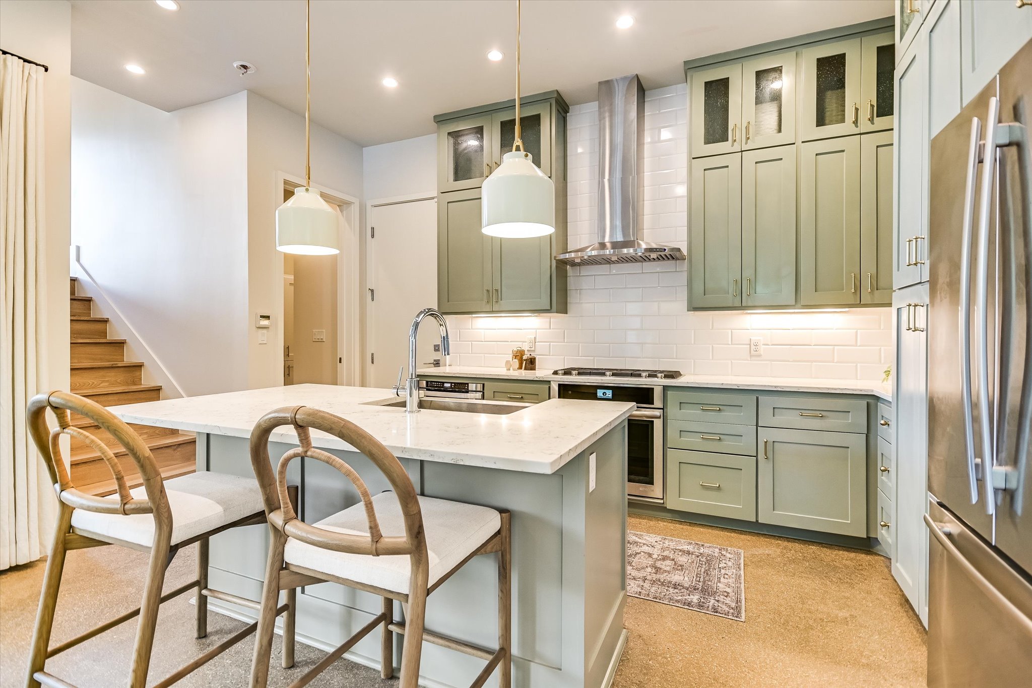 1605 Hether Street Austin, TX 78704 - Photo 11 of 26 Modern kitchen featuring a central island with integrated sink, light-toned countertops, sage green cabinetry, stainless steel appliances, and subway tile backsplash