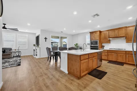 a kitchen with stainless steel appliances granite countertop wooden cabinets a sink a stove a dining table and chairs
