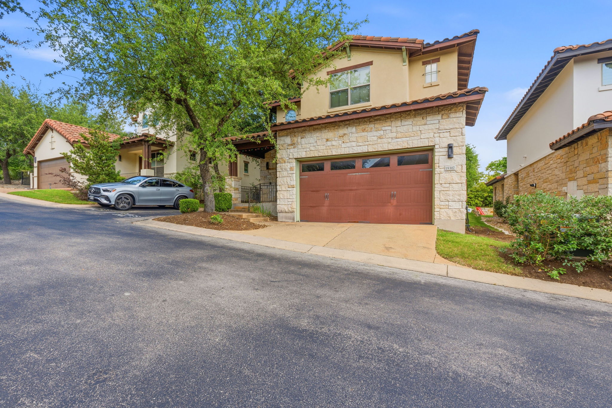 15317 Falconhead Grove Loop Austin, TX 78738 - Photo 35 of 36 Stucco and stone facade home featuring a two-car garage with a brown door, terracotta roof tiles, and an integrated outdoor sconce