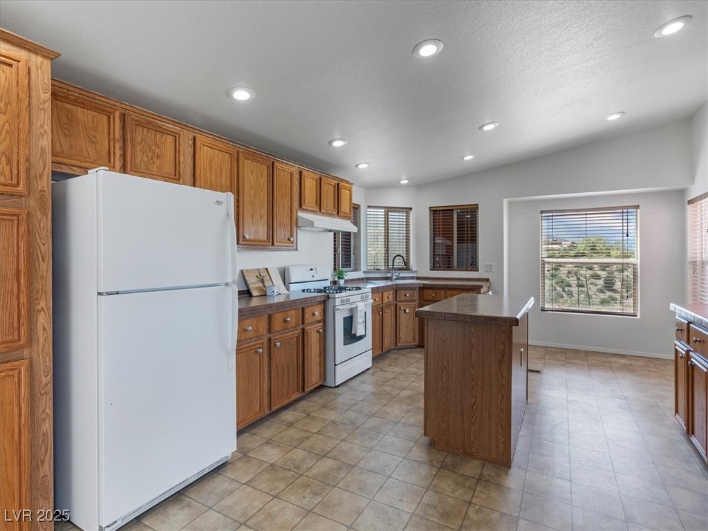70 West Bonanza Road Las Vegas, NV 89124 - Photo 19 of 71 Kitchen featuring white appliances, under cabinet range hood, brown cabinetry, recessed lighting, and a kitchen island