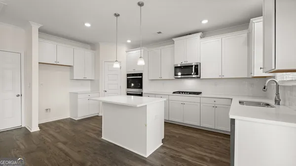 a large kitchen with granite countertop a stove a sink a center island and wooden floor