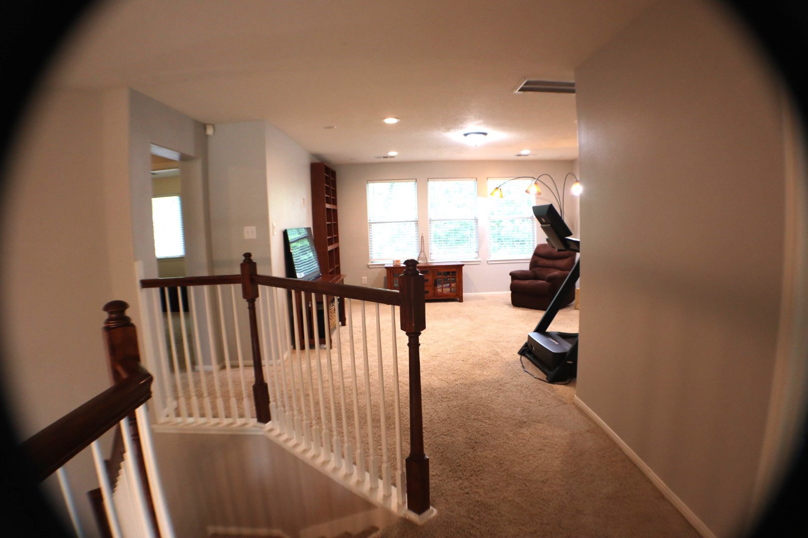 19114 Emory Trail Spring, TX 77388 - Photo 18 of 32 Aa cozy, carpeted view of the game room area with ample natural light from large windows. It features enough space for comfortable seating arrangement, a treadmill, and built-in shelving, accessed by a staircase with wooden handrails.