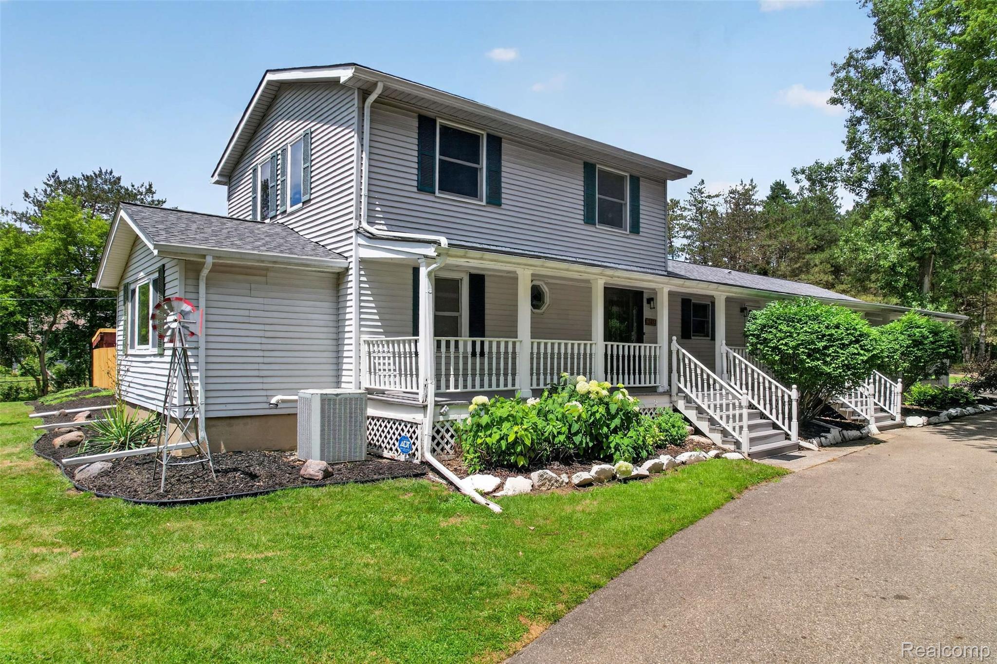 Two-story home with light gray siding, dark green shutters, and a covered front porch featuring white railings