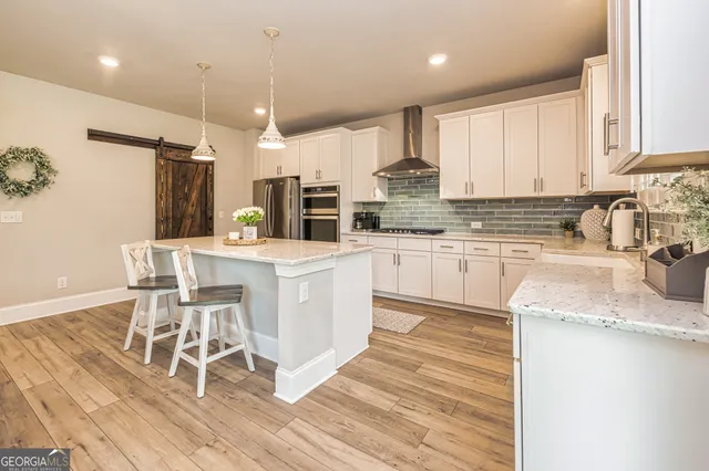 a kitchen with stainless steel appliances kitchen island granite countertop a refrigerator a stove a sink and white cabinets with wooden floor