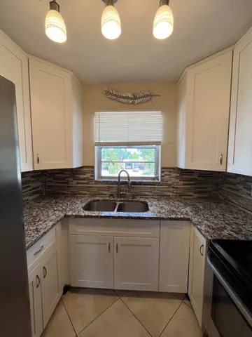 a kitchen with granite countertop a sink a stove top oven and cabinetry