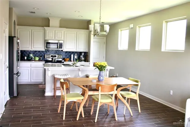 a kitchen with stainless steel appliances kitchen island granite countertop a dining table chairs and a refrigerator