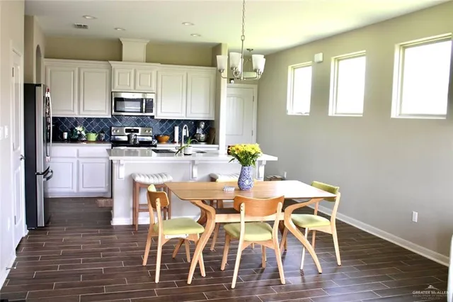 a kitchen with stainless steel appliances kitchen island granite countertop a dining table chairs and a refrigerator