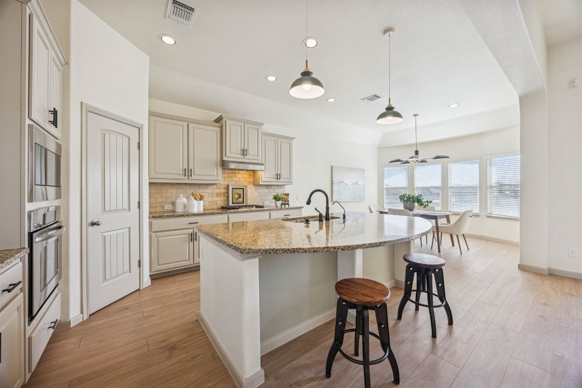 3329 Eagle Ridge Lane Pflugerville, TX 78660 - Photo 11 of 35 Kitchen with decorative backsplash, light stone counters, a breakfast bar area, an island with sink, and decorative light fixtures