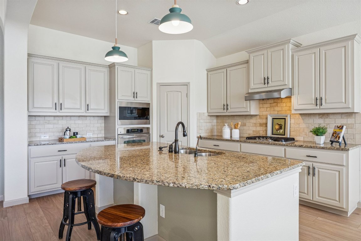 3329 Eagle Ridge Lane Pflugerville, TX 78660 - Photo 12 of 35 Kitchen featuring light wood-style flooring, a kitchen island with sink, a kitchen bar, light stone counters, and tasteful backsplash