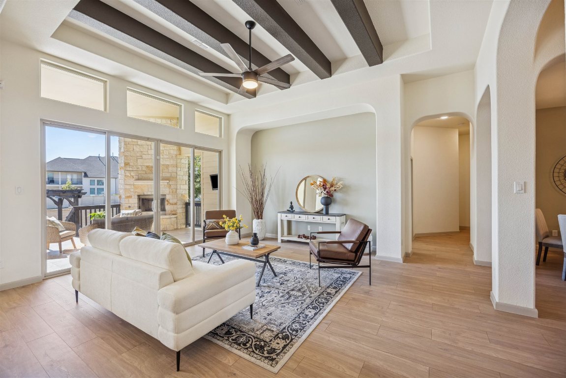 3329 Eagle Ridge Lane Pflugerville, TX 78660 - Photo 7 of 35 Living area featuring beamed ceiling, ceiling fan, arched walkways, light wood-style flooring, and a stone fireplace