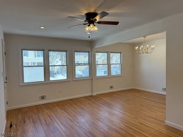 an empty room with wooden floor chandelier fan and windows