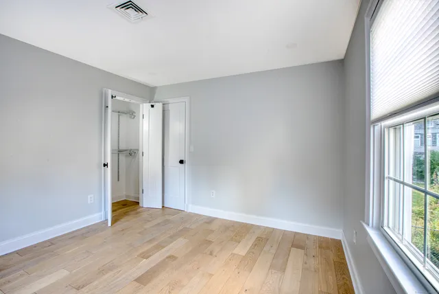a view of an empty room with wooden floor and a window