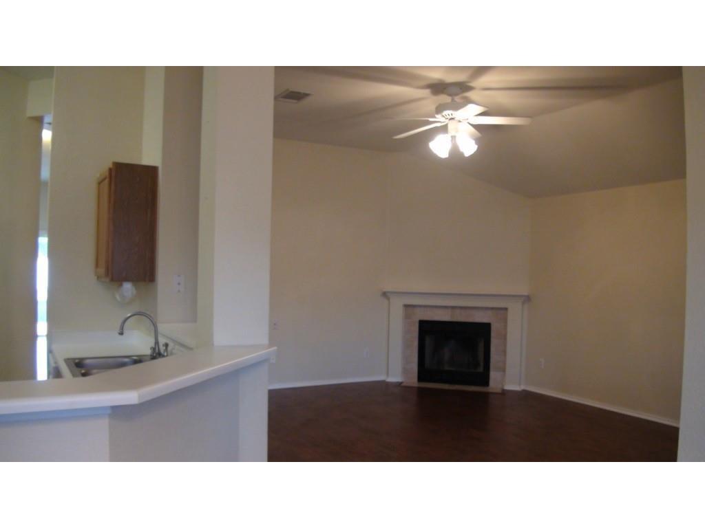 13915 Randalstone Drive Pflugerville, TX 78660 - Photo 2 of 19 Unfurnished living room with a ceiling fan, dark wood-style flooring, a tiled fireplace, and vaulted ceiling