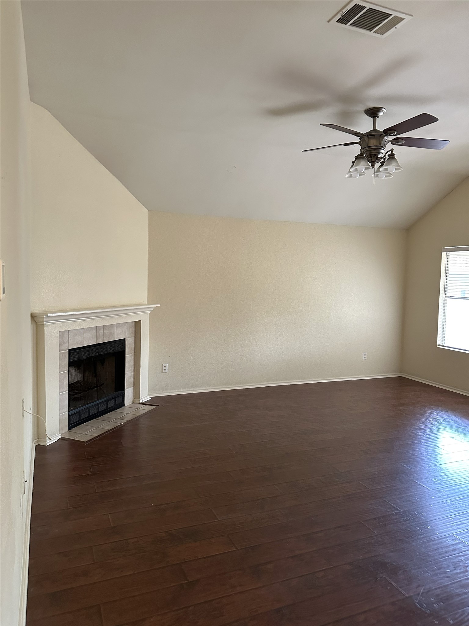 13915 Randalstone Drive Pflugerville, TX 78660 - Photo 3 of 19 Unfurnished living room with vaulted ceiling, a ceiling fan, a fireplace, and dark wood-style floors