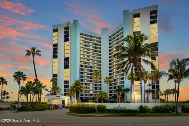 a front view of multi story residential apartment building with a yard and palm trees